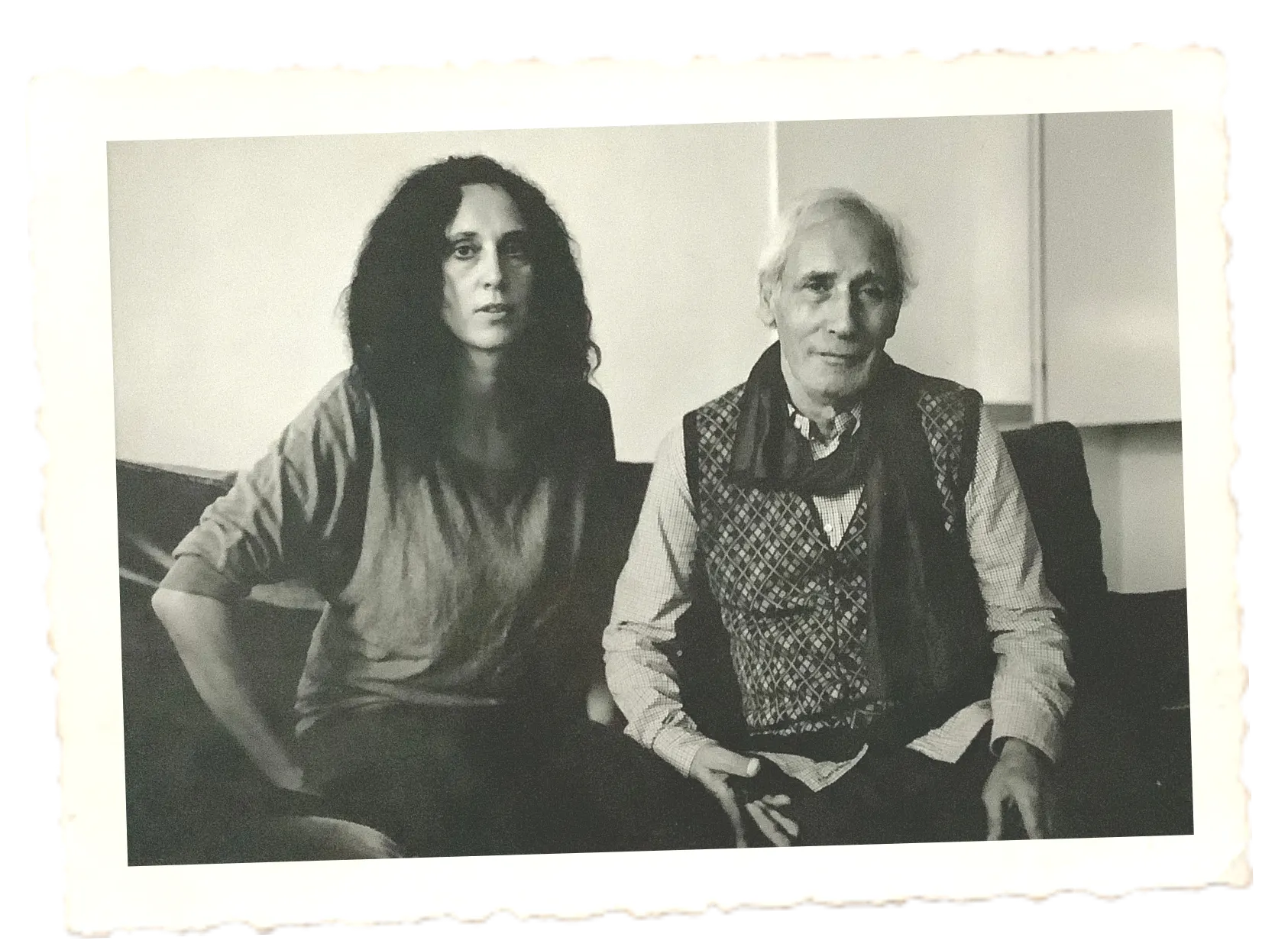 Eine Schwarzweißaufnahme von Helena, die Bestatterin von Atelier Magnolia Bestattungen, neben einem eleganten lächelndem Mann, auf einem Sofa sitzend