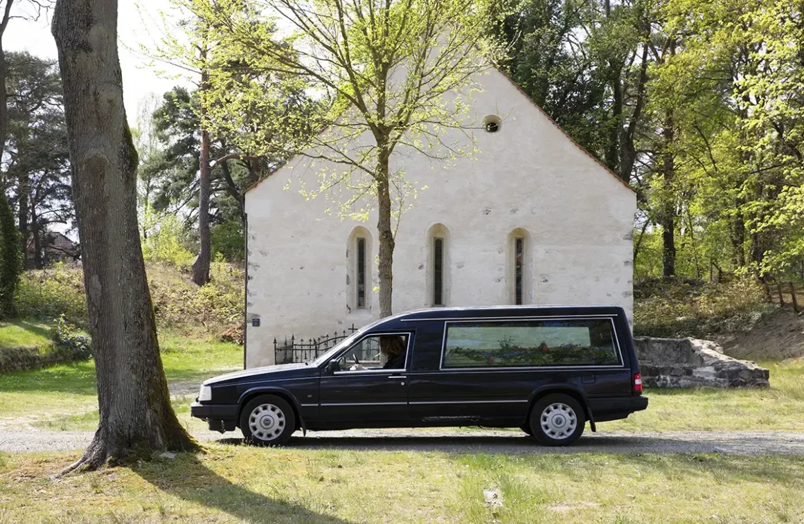 Ein altes Leichenwagen von Volvo steht vor einer weißen Kirchenkapelle