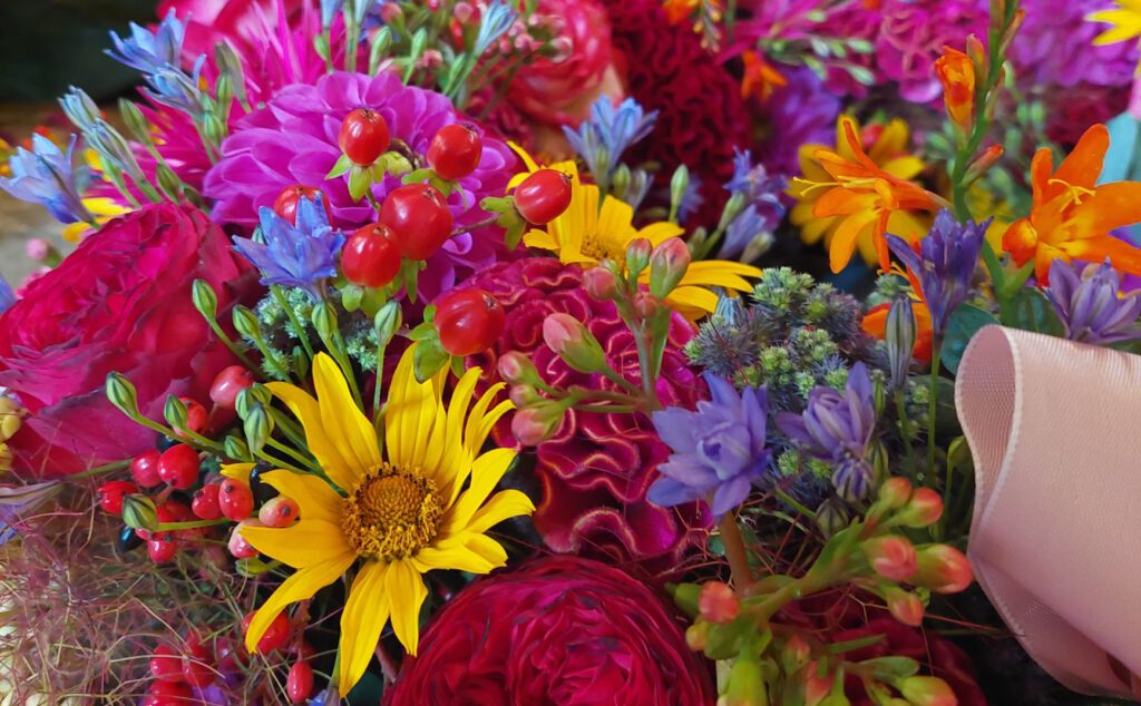 Bildfüllende Detailaufnahme eines Blumengestecks in kräftigem Pink, Lila , Orange, Rot und Gelb mit verschiedenen Blüten und Beeren