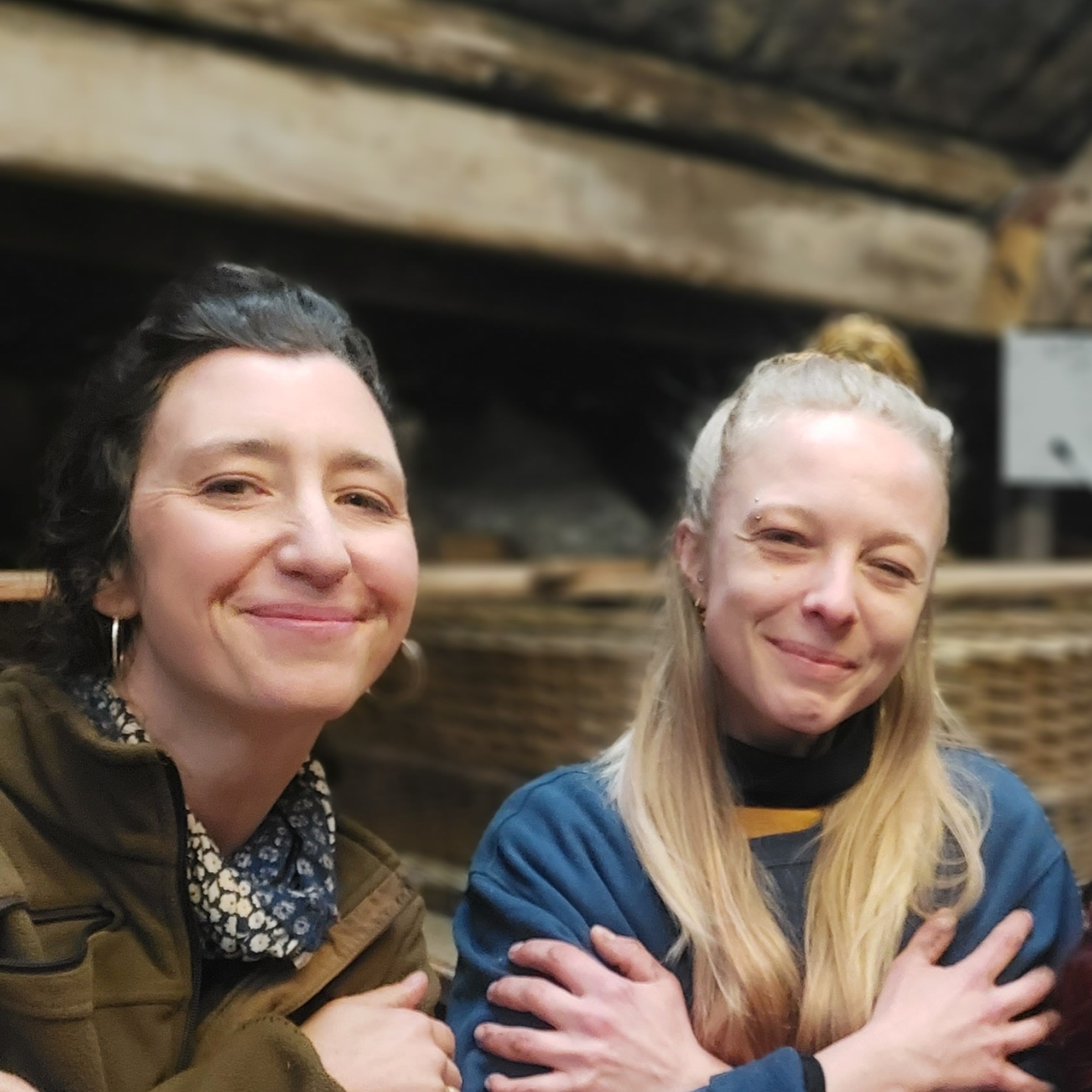 Die Sargflechterinnen Sophia und Abi von Bestatter Team Ateleir Magnolia Bestattungen in Berlin lächeln in die Kamera. Im Hintergrund sieht man einen Sarg aus Weide.