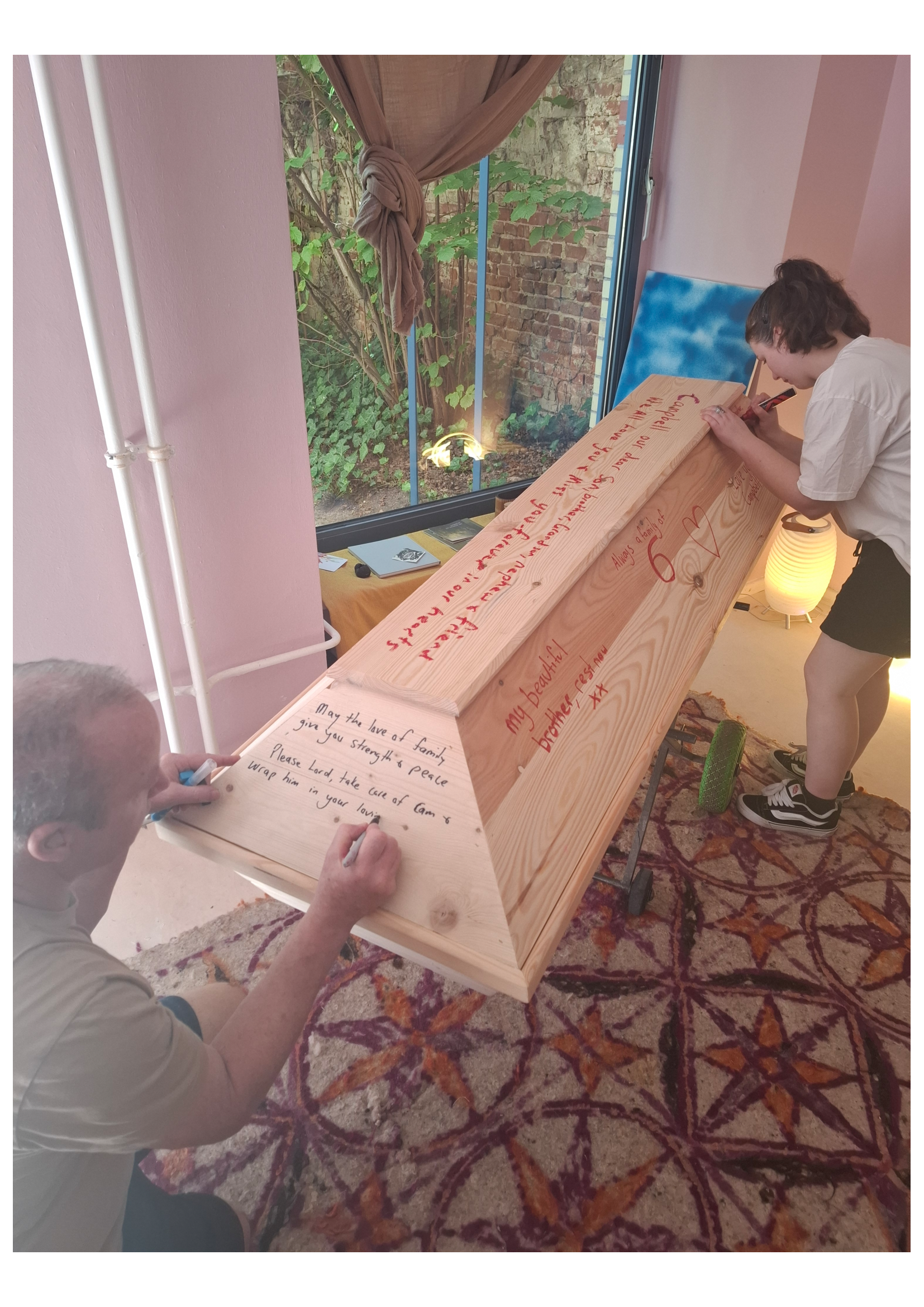 Ein Mann und eine Frau schreiben auf einem geschlossenen Holz Sarg. Eine Momentaufnahme von einer Trauerfeier in Atelier Magnolia Bestattungen in Berlin Mitte