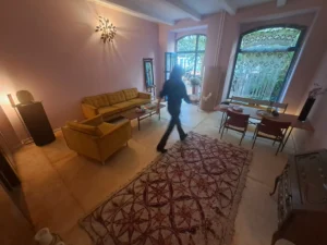 Ein schwarz angezogenen Mensch läuft durch ein Zimmer mit rosafarbenen Wänden