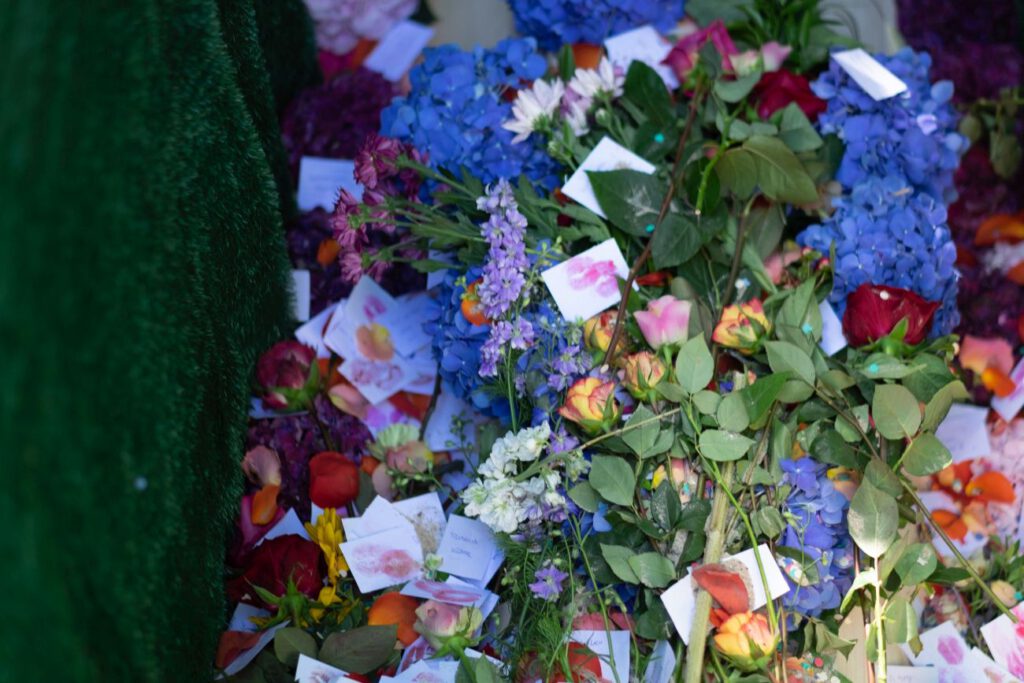 Detail Draufsicht auf ein mit bunten Blumen und Kärtchen mit Lippenstiftabdrücken gefülltes Grab