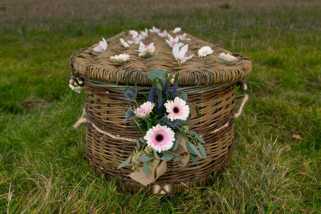 Ein Sarg aus Weide mit weiße kleine Wiesenblumen auf einem grünen Feld