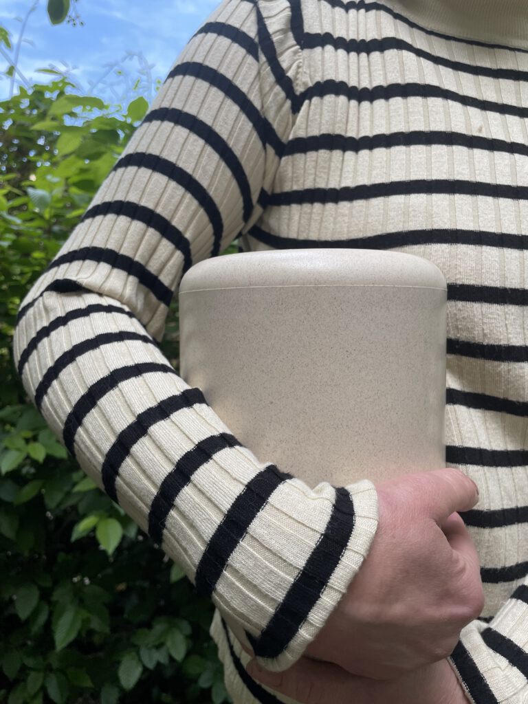Eine Person mit einem gestreiften Pullover hält eine Urne in den Arm
